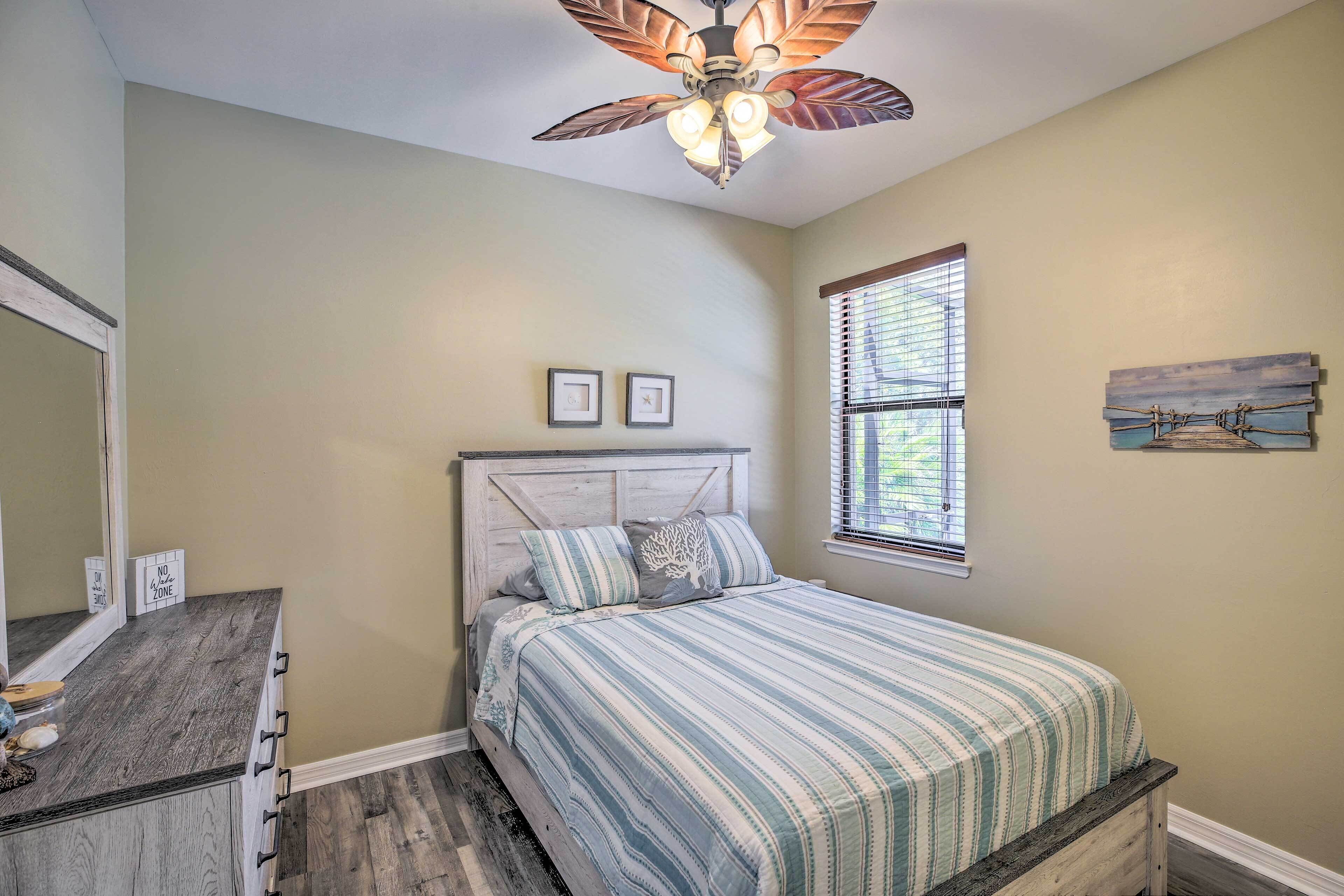 A bedroom with a bed, a dresser, a ceiling fan, a window with blinds, and wall art.