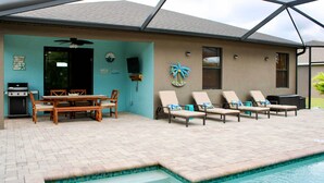 A pool area with lounge chairs, a table, and a grill. - Pool & Lanai: Centrally Located Cape Coral Home (Cape Coral)