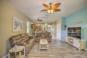 A spacious living room with a large sectional sofa, a coffee table, and a TV on a wooden cabinet. There are ceiling fans and a beach-themed wall art. - Pool & Lanai: Centrally Located Cape Coral Home (Cape Coral)