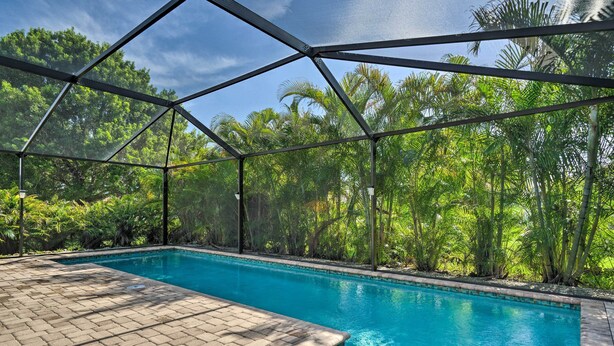 A swimming pool with a clear view of the surrounding lush greenery and a metal roof structure. - Pool & Lanai: Centrally Located Cape Coral Home (Cape Coral)