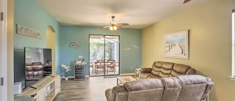 A living room with a sofa, a TV, and a ceiling fan. There is a sliding glass door leading to a patio area.