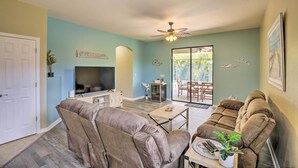 A living room with a sofa, a TV, a ceiling fan, and a sliding glass door leading to an outdoor area. - Pool & Lanai: Centrally Located Cape Coral Home (Cape Coral)