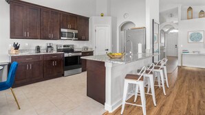 A modern kitchen with dark wood cabinets, a central island with bar stools, a microwave, stove, and a refrigerator. - Davenport Vacation Home w/ Pool, Spa & Game Room! (Davenport)