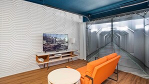 A modern room with a patterned wall, a flat-screen TV, a small table, and an orange chair. - Davenport Vacation Home w/ Pool, Spa & Game Room! (Davenport)
