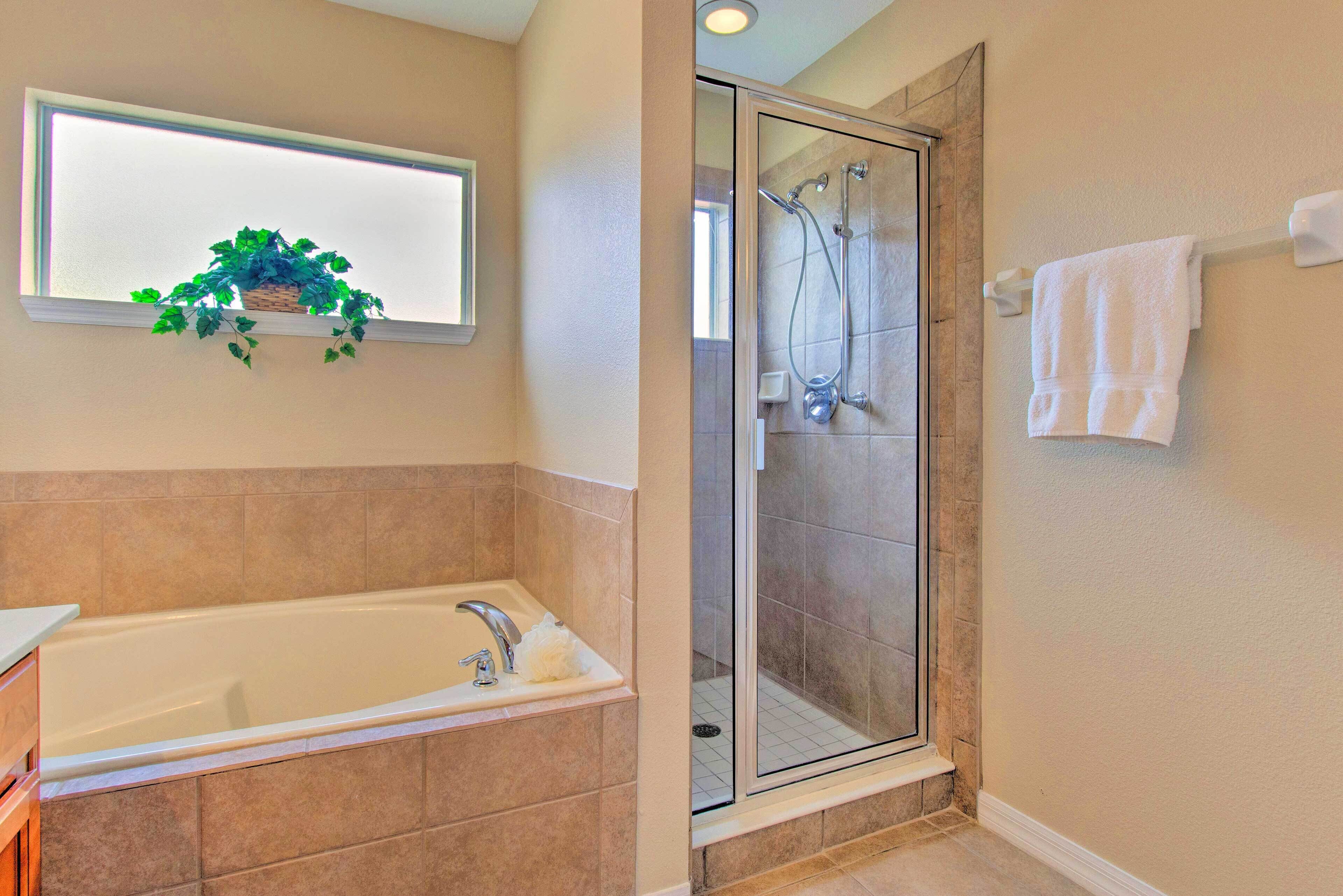Une salle de bain avec une baignoire, une douche à parois de verre et une fenêtre agrémentée d’une plante.