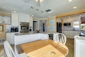 A modern kitchen with white cabinetry, a central island, and a dining area with a wooden table and chairs. - Waterfront Oasis! Heated Pool, 2 Docks & Boat Lift (Palmetto)