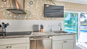 Una cocina moderna con encimera de granito, electrodomésticos de acero inoxidable y un televisor de pantalla plana sobre el fregadero.