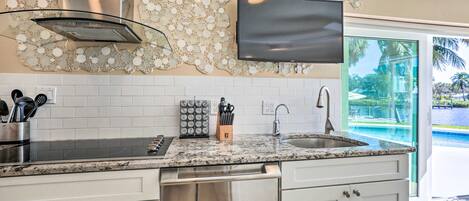 A modern kitchen with a granite countertop, stainless steel appliances, and a flat-screen TV mounted above the sink.