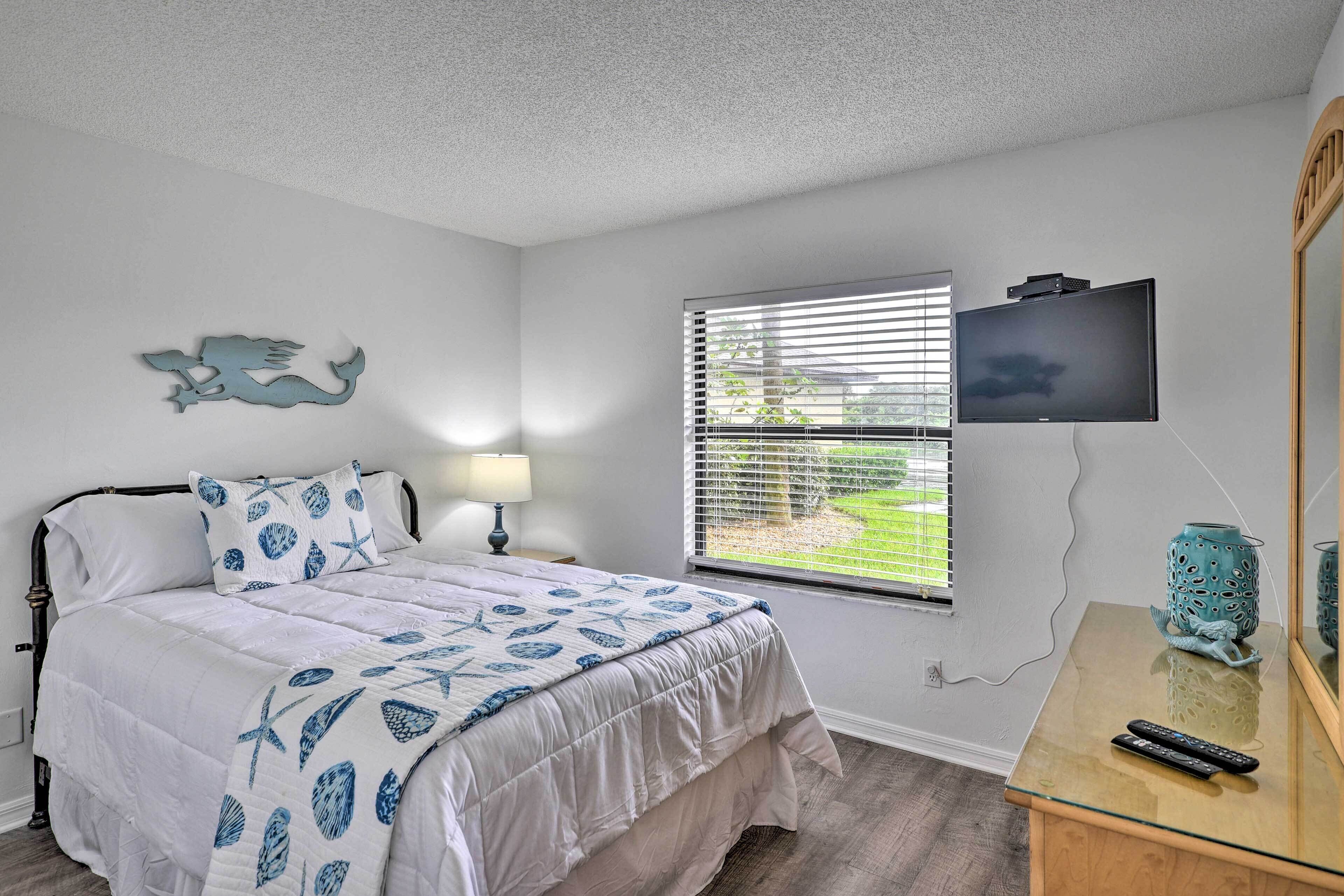 A bedroom with a bed, a TV, a window with blinds, and a decorative fish on the wall.