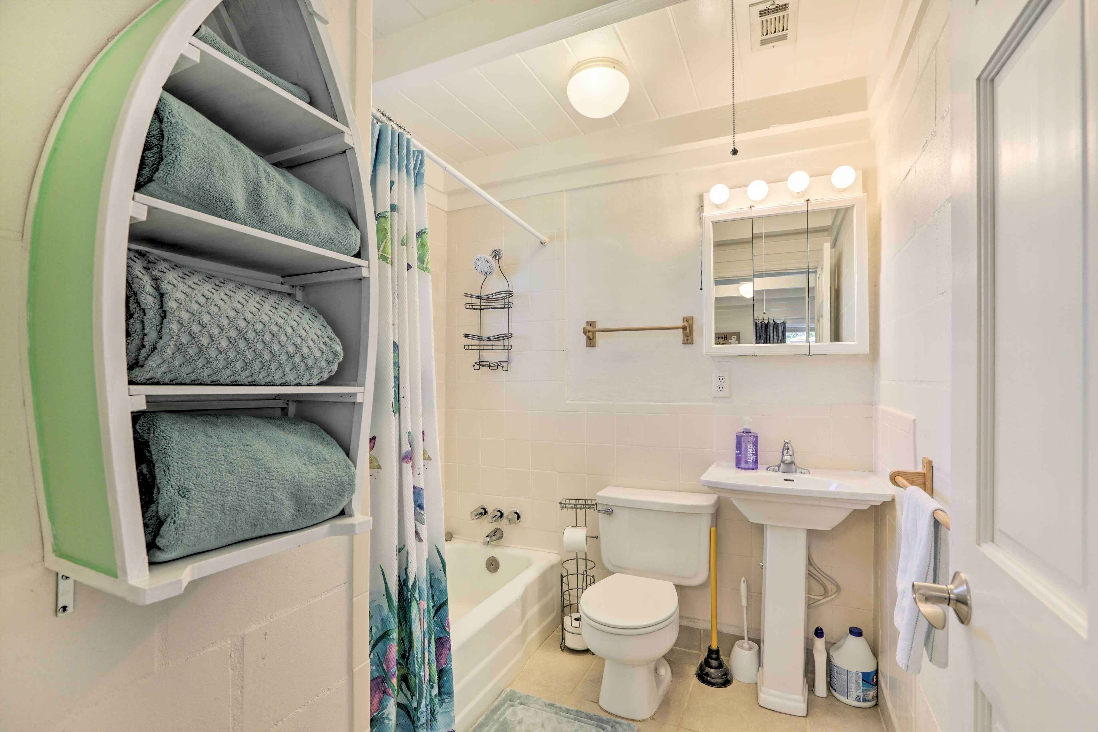 A bathroom with a bathtub, toilet, sink, and a mirror with lights.