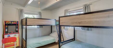 A room with bunk beds, a small table with a video game, and a window with curtains.