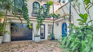 A courtyard with a brick floor, a large black gate, and lush greenery including ferns and potted plants. - South Tampa Studio in Desirable Historic District! (Tampa)