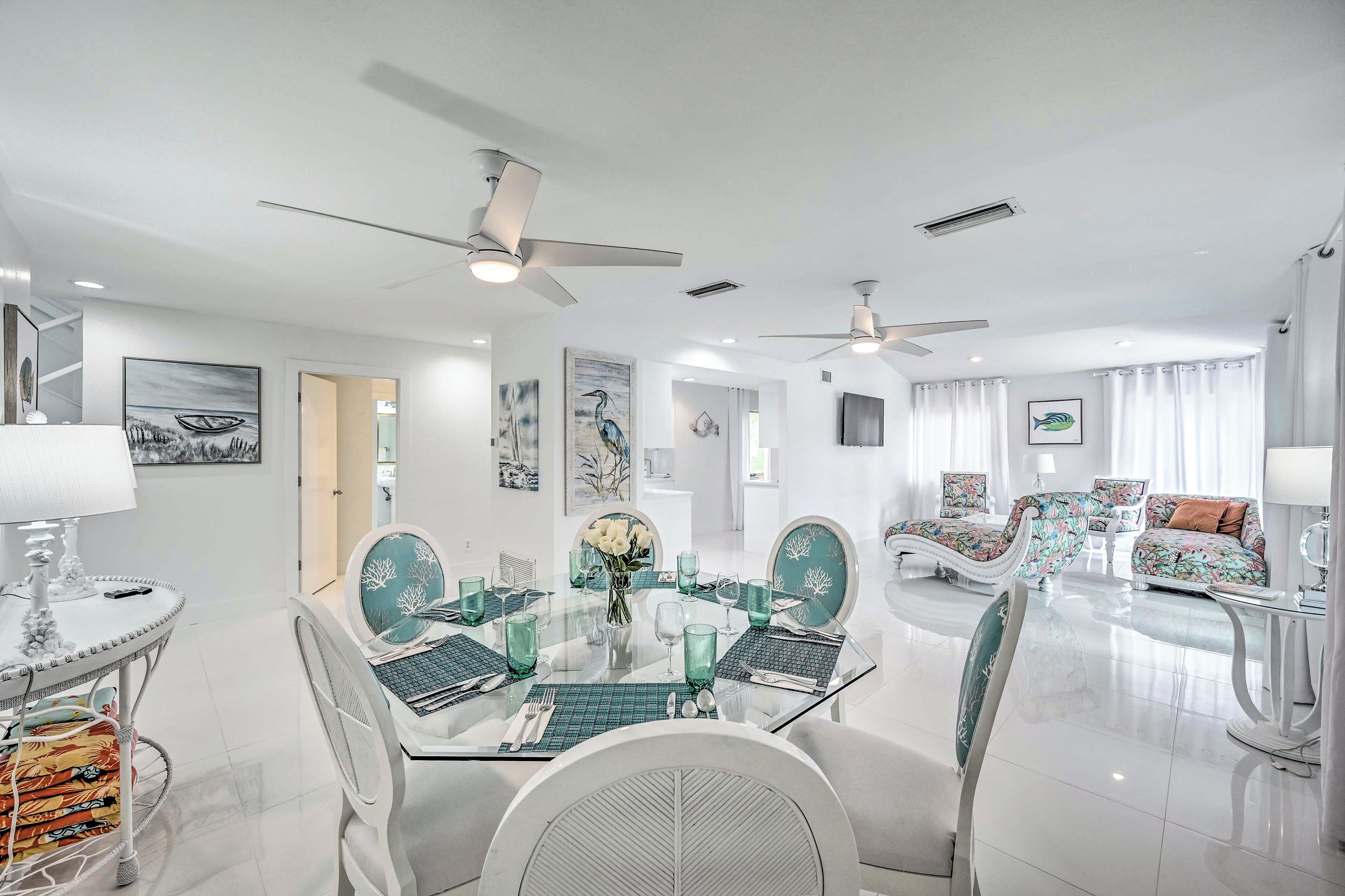 A modern dining area with a glass table, white chairs, and ceiling fans.