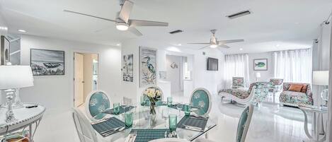 A modern dining area with a glass table, white chairs, and ceiling fans.