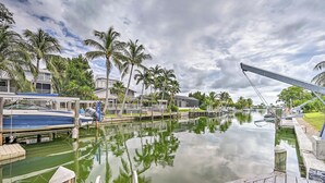 A marina with docked boats, a wooden deck, and a calm water body reflecting palm trees and buildings. - Waterfront Marco Island House With Shared Dock! (Marco Island)
