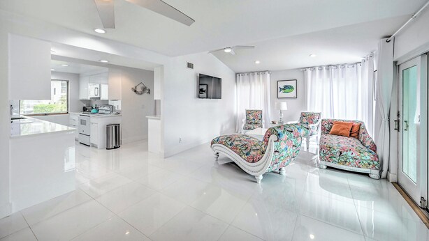 A modern living room with a sofa and a coffee table, a kitchen area with white cabinets, and a ceiling fan. - Waterfront Marco Island House With Shared Dock! (Marco Island)