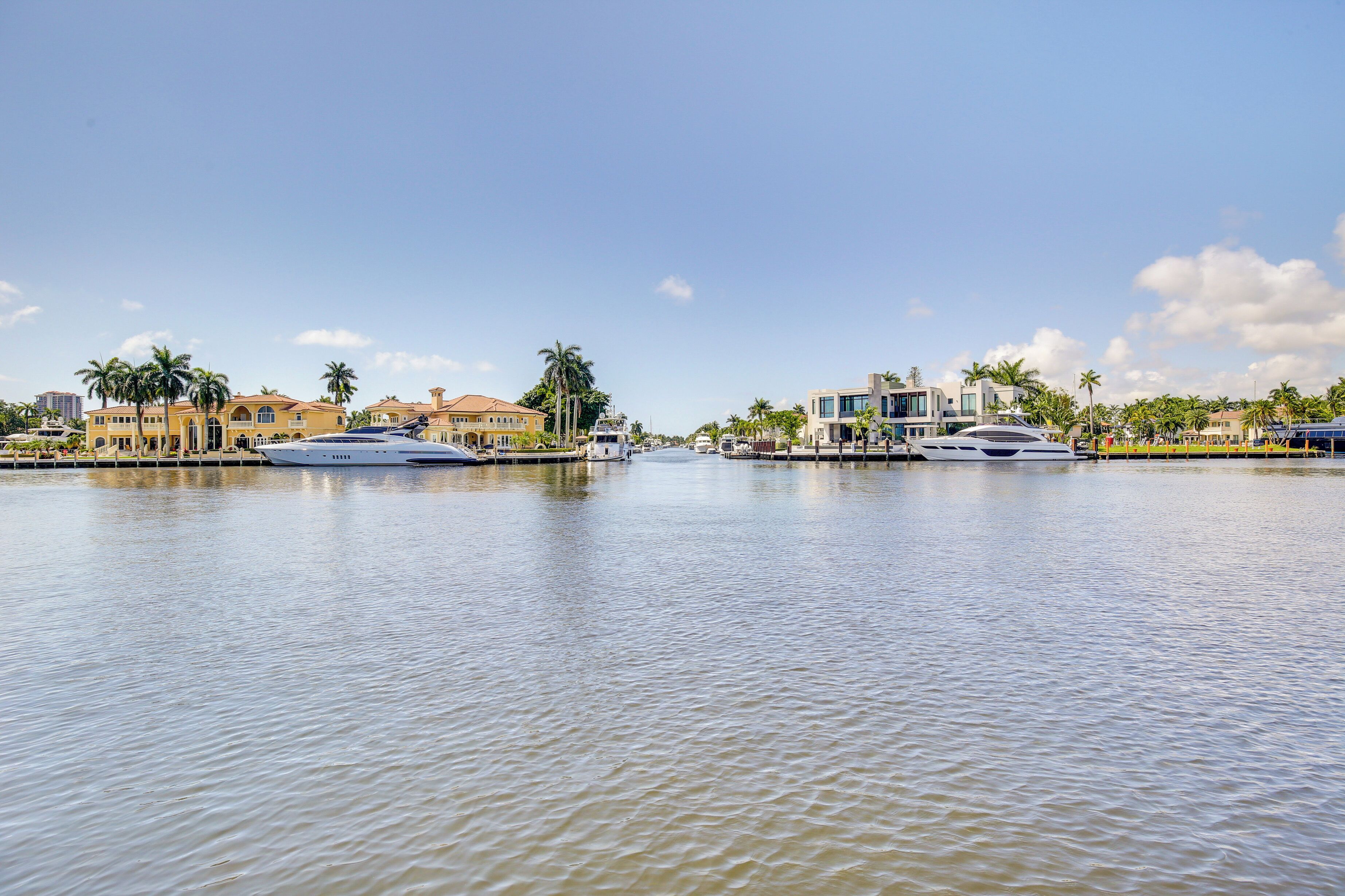 Une propriété située au bord de l’eau, avec plusieurs bateaux amarrés, comprenant un port de plaisance et des villas de luxe bordées de palmiers.