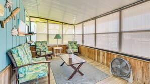Une pièce chaleureuse avec des murs en bois, une grande fenêtre et un ventilateur. On y trouve deux chaises, une table et une lampe.