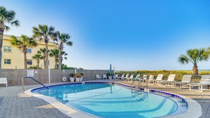 Una piscina con borde de azulejos, rodeada de sillas de descanso y palmeras, con vista al océano al fondo.