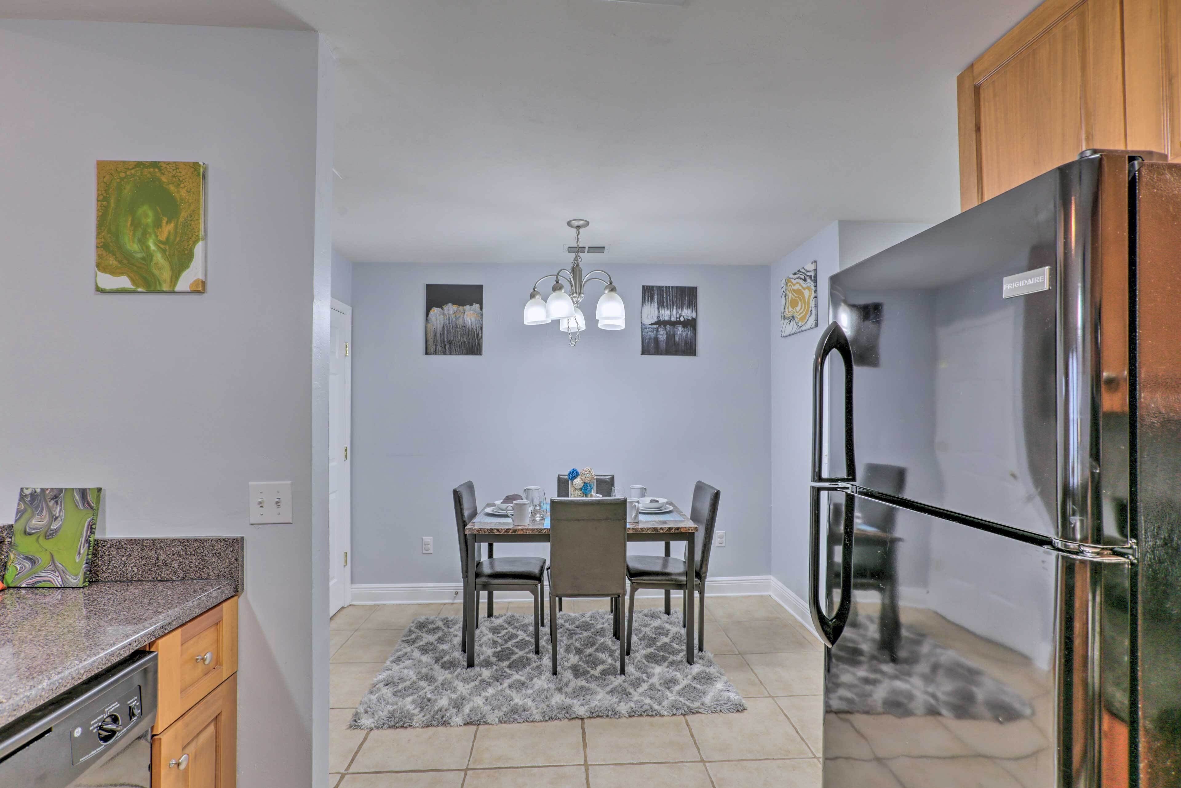 A modern kitchen with a dining table, chairs, a refrigerator, and artwork on the walls.