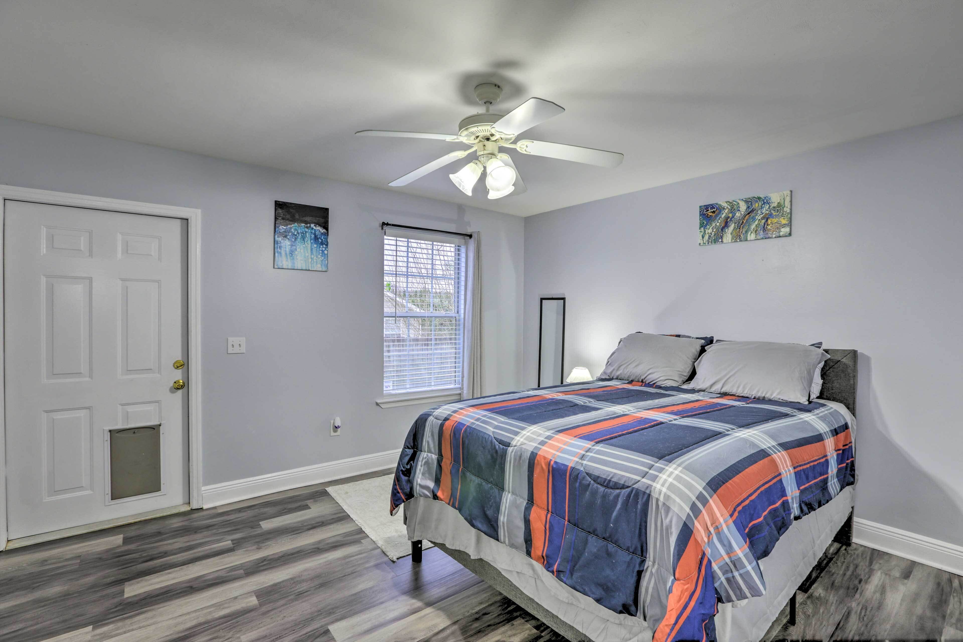 A bedroom with a bed, a ceiling fan, a window with blinds, and a door.