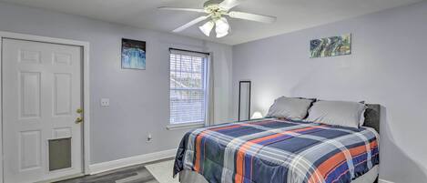 A bedroom with a bed, a ceiling fan, a window with blinds, and a door.