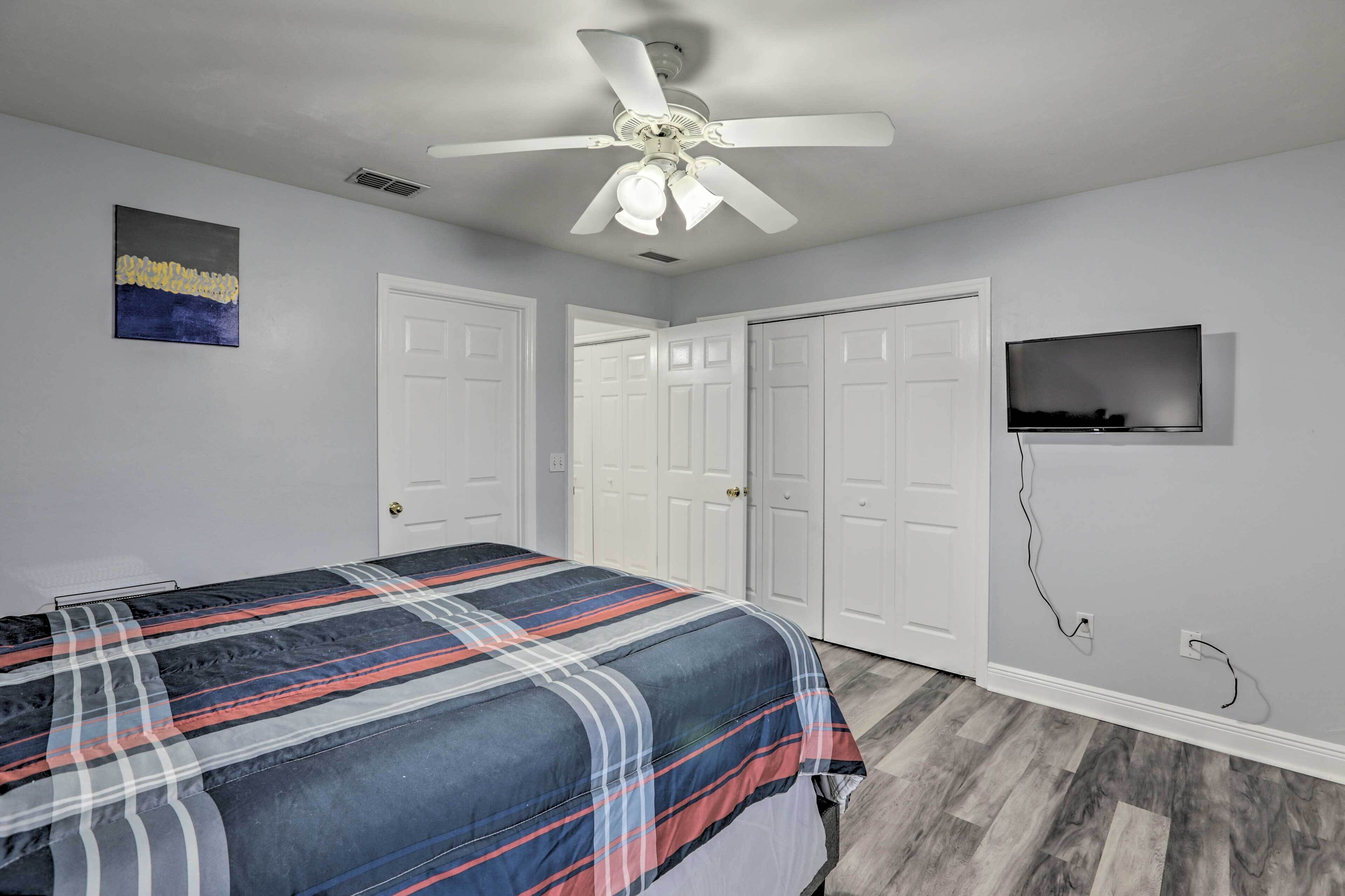A bedroom with a bed, a ceiling fan, a TV, and a door.