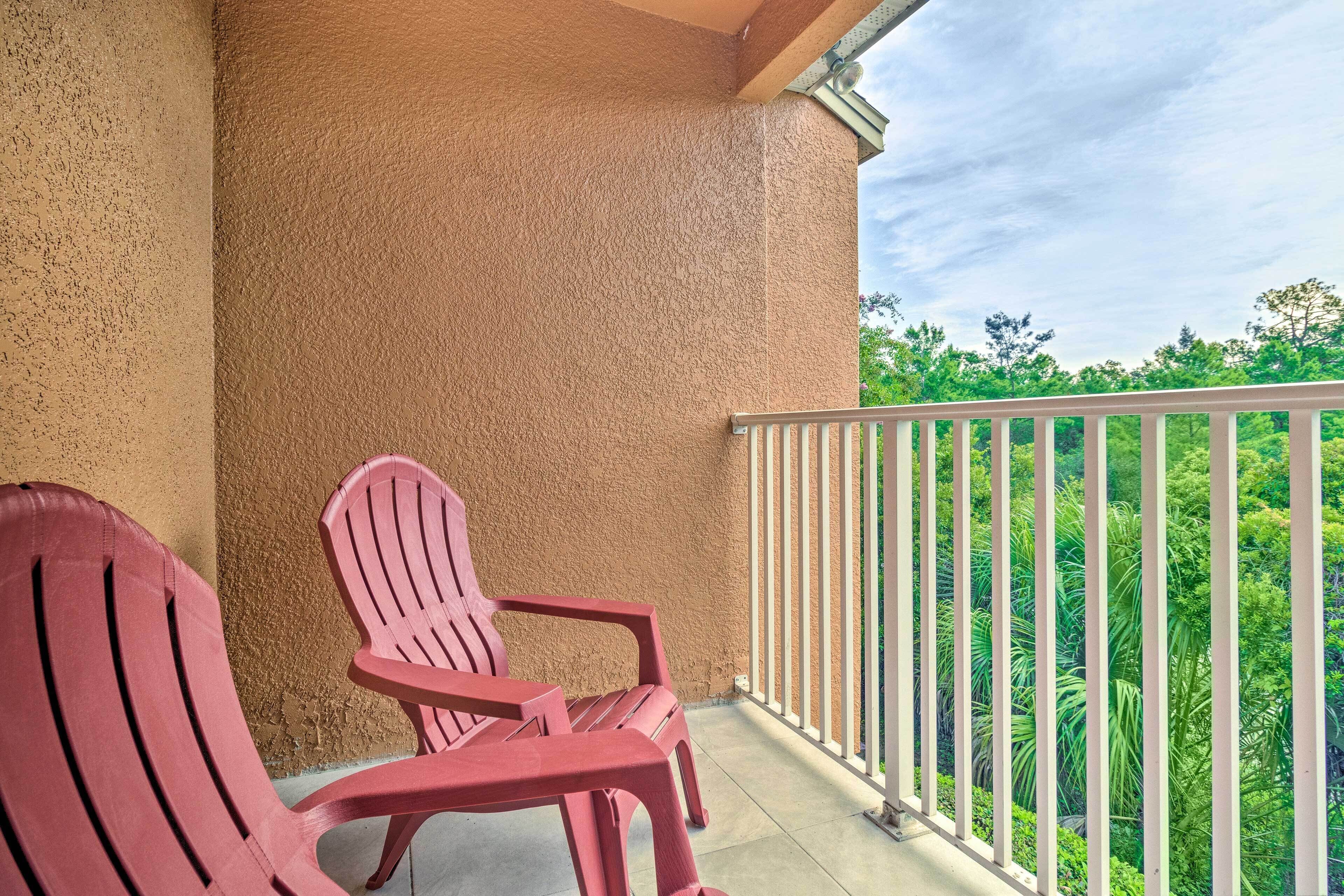 A balcony with two red chairs, a textured wall, and a railing overlooking a lush green landscape.