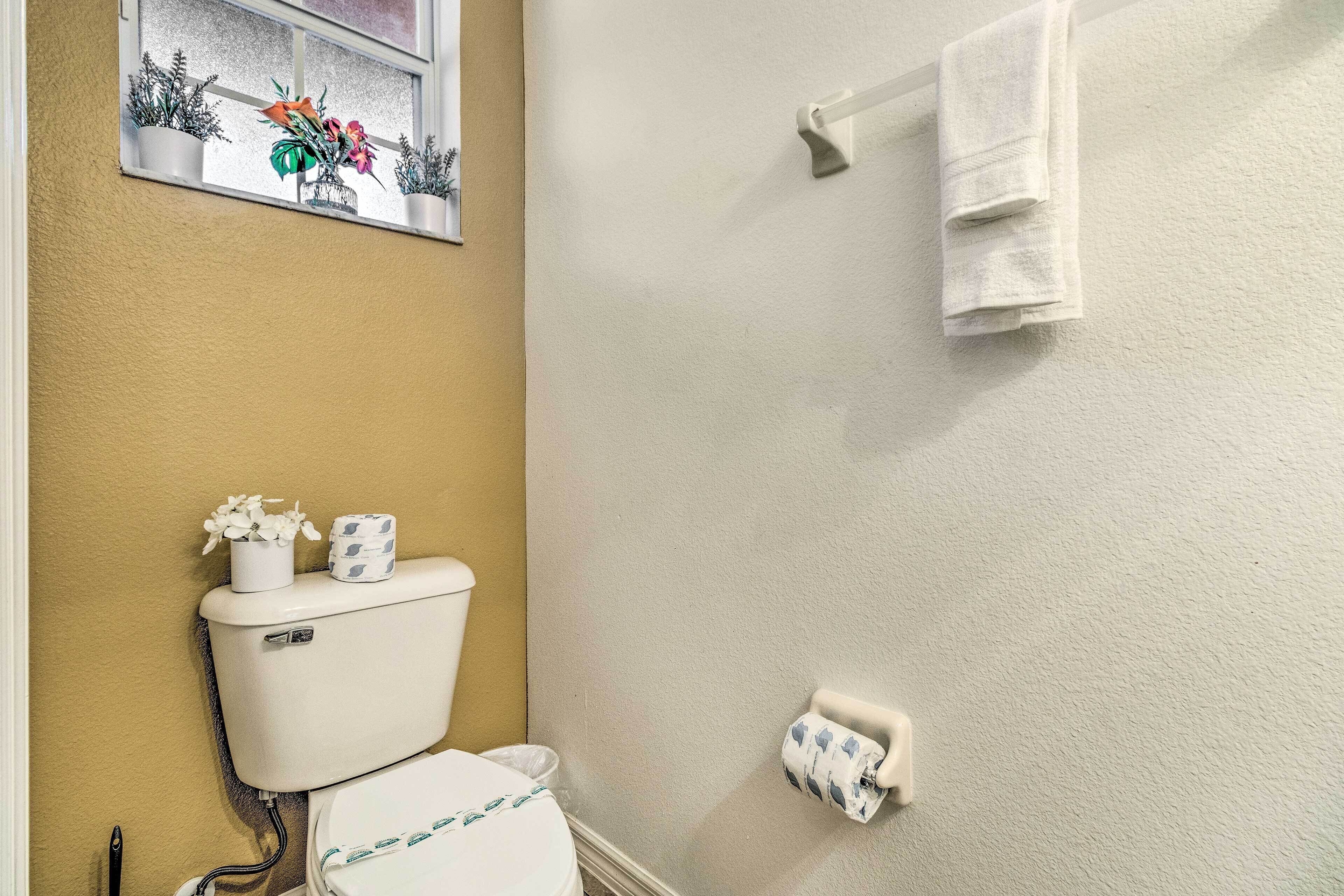 A bathroom with a toilet, a towel rack, a toilet paper holder, and a window with a plant decoration.