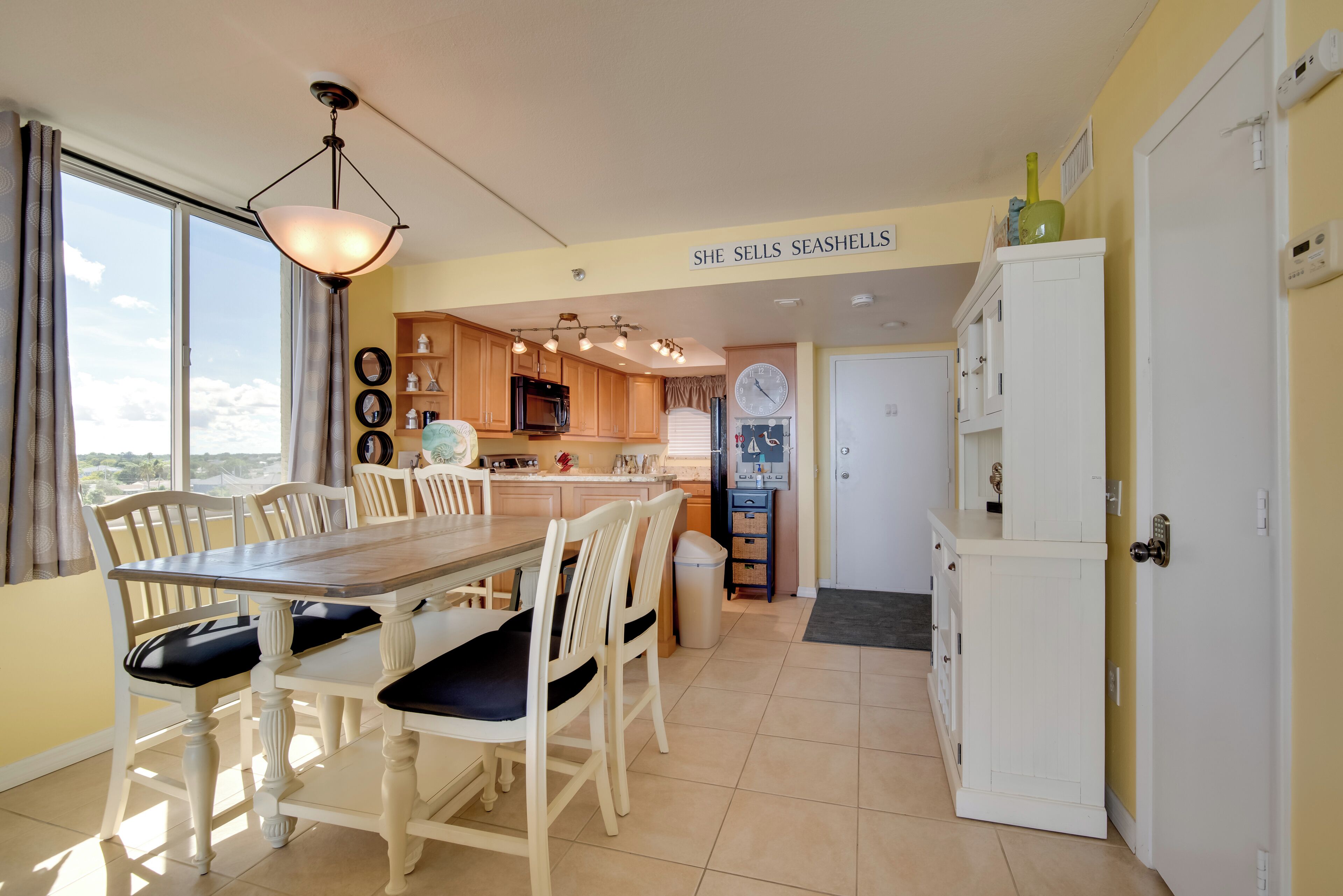 A kitchen with a dining area, wooden cabinets, a clock, and a sign above the cabinets.