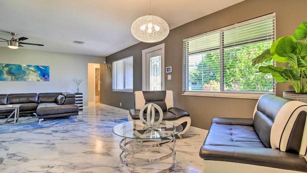 A modern living room with a glass coffee table, leather sofas, and a ceiling fan. - Wilton Manors Home w/ Pool ~ 4 Mi to Beach! (Wilton Manors)