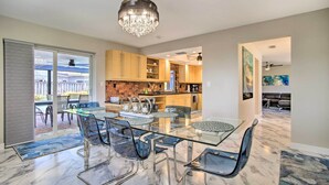 A modern kitchen with a glass dining table and chairs, a chandelier, and a view to the outside. - Wilton Manors Home w/ Pool ~ 4 Mi to Beach! (Wilton Manors)