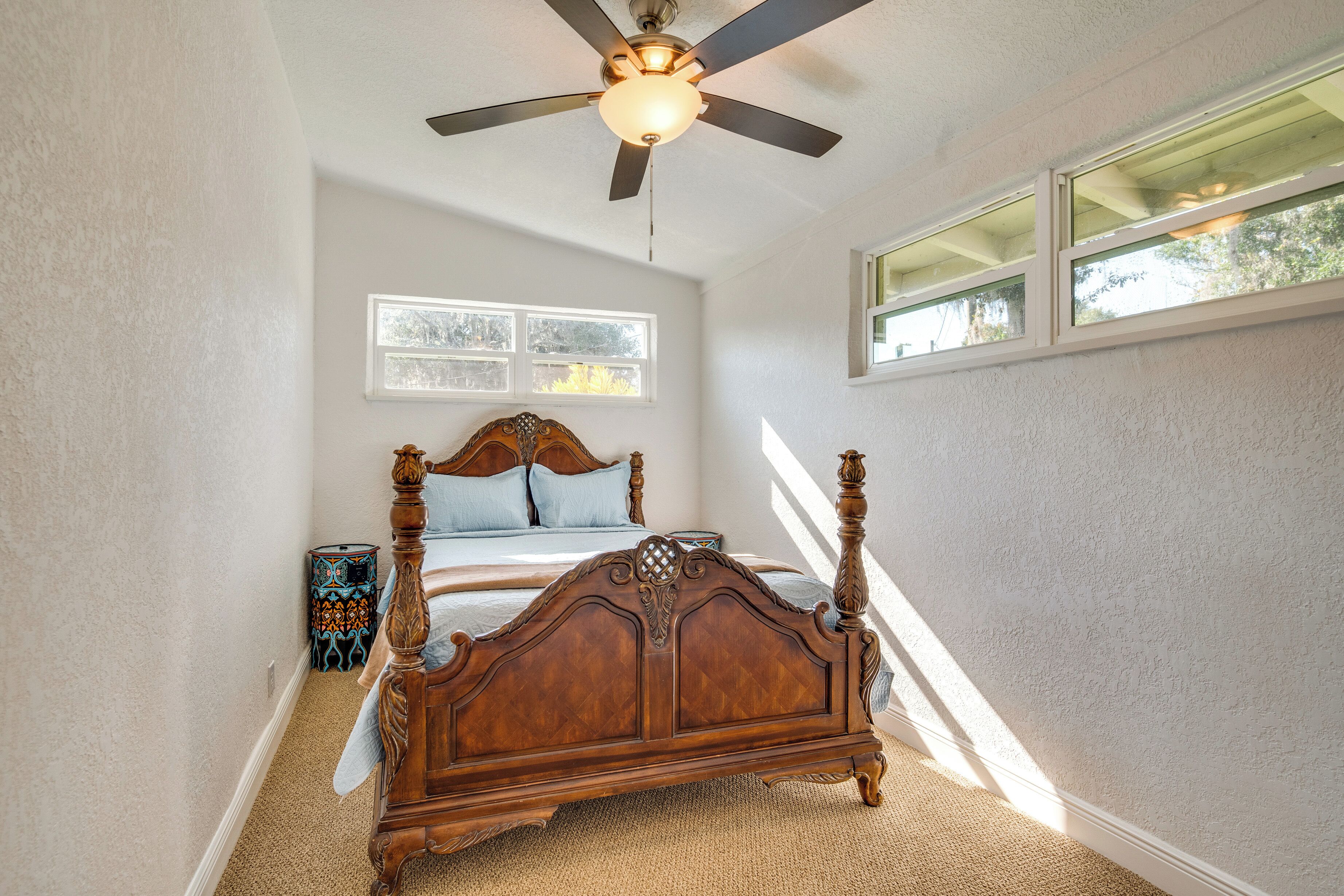 A bedroom with a wooden four-poster bed, a ceiling fan, and a window with blinds.