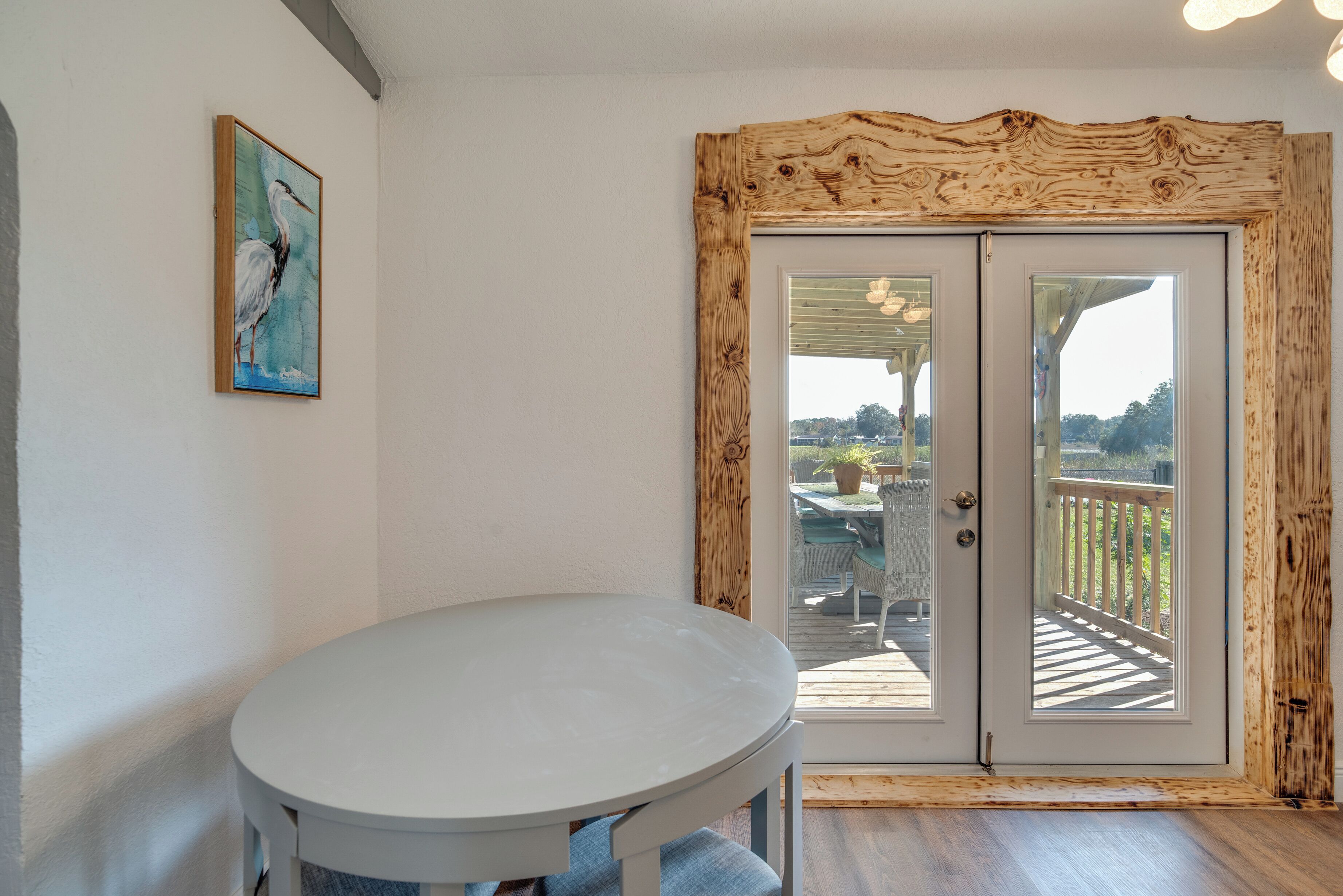 A room with a round table, a wooden-framed door leading to an outdoor deck, and a painting on the wall.