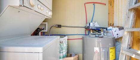 Un cuarto de servicio pequeño y funcional, con lavadora, calentador de agua grande y cableado eléctrico expuesto.