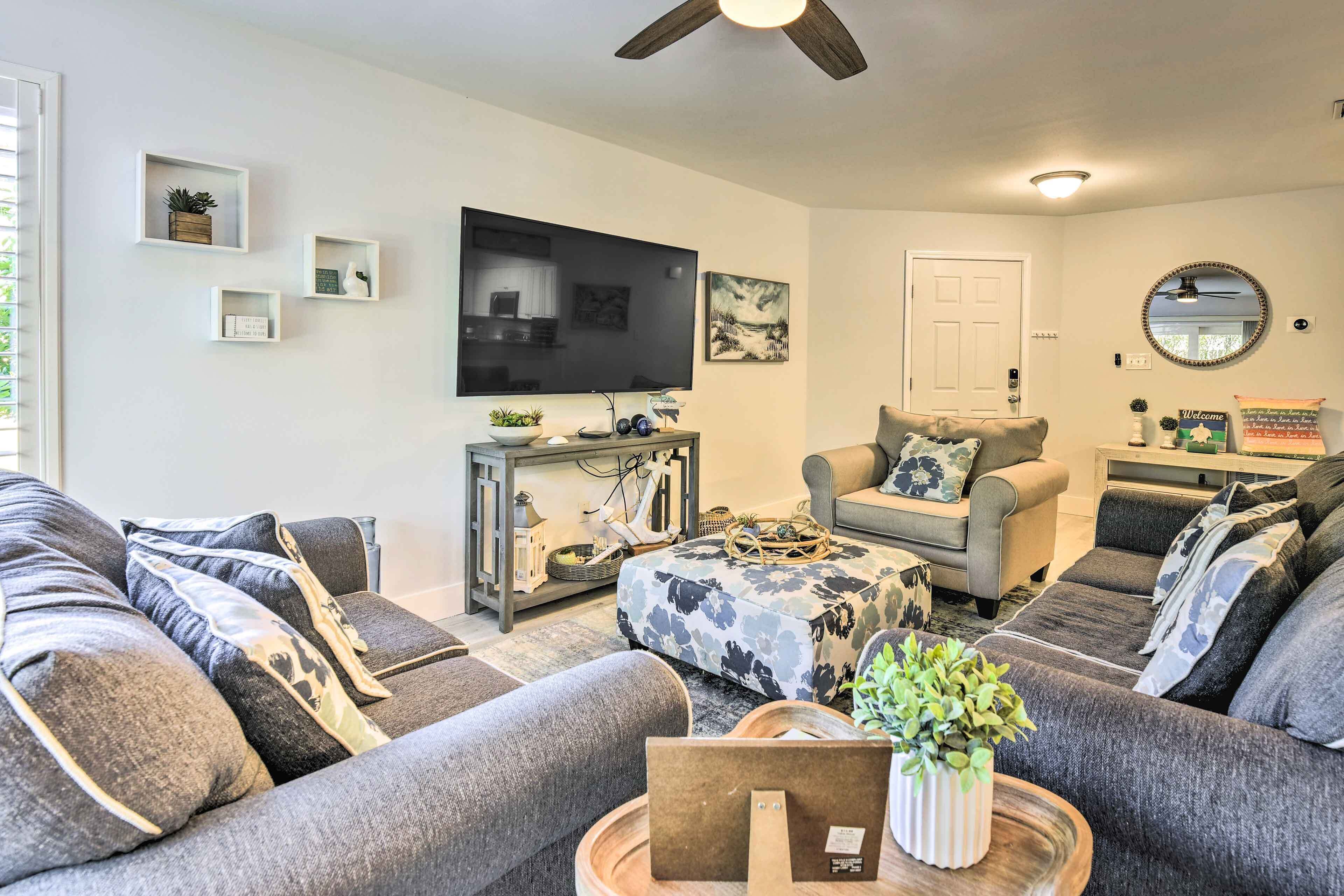 A modern living room with grey sofas, a coffee table with a plant, a TV, and a ceiling fan.
