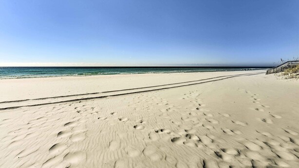 A sandy beach with footprints leading to the water, a clear sky, and a distant shoreline. - 'tipsy Turtle' Condo w/ Patio & Harbor Access (Destin)