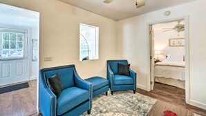 A room with two blue armchairs, a patterned rug, a ceiling fan, and a bed in the adjacent room. - Tropical Port Charlotte Cottage - Walk to Bay! (Punta Gorda)