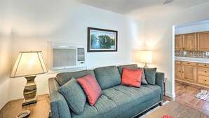A living room with a sofa, two lamps, a framed picture on the wall, and a kitchen area visible through an open doorway. - Tropical Port Charlotte Cottage - Walk to Bay! (Punta Gorda)