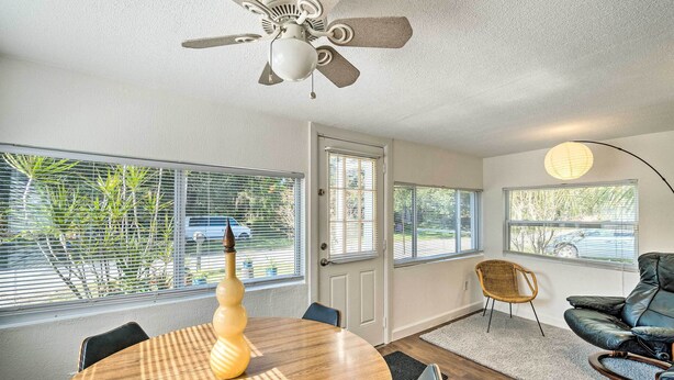 A dining area with a round table, chairs, a ceiling fan, and large windows with blinds. - Tropical Port Charlotte Cottage - Walk to Bay! (Punta Gorda)