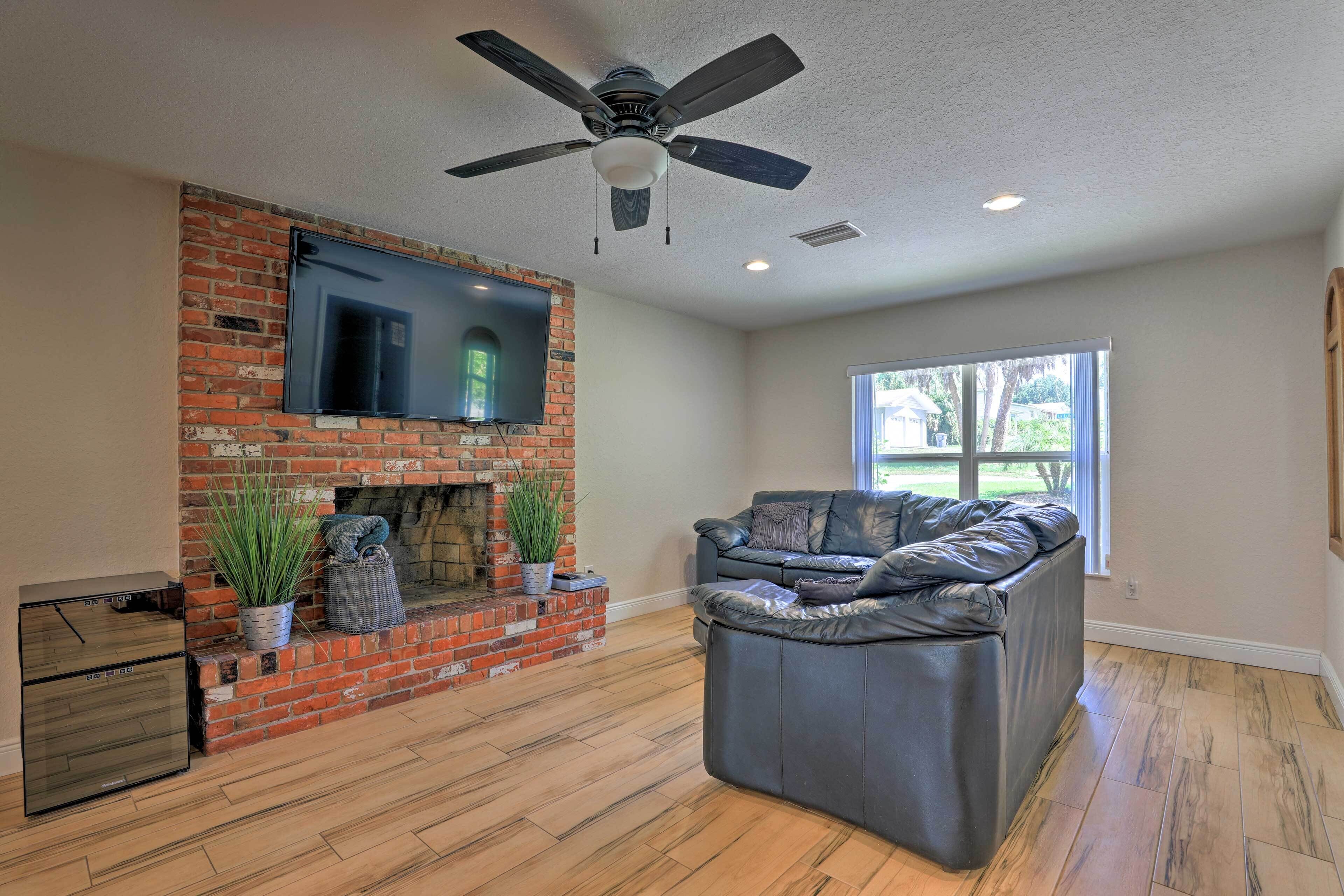 A living room with a brick fireplace, a flat-screen TV mounted above it, a leather sofa, and a ceiling fan.