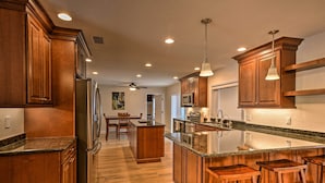 A modern kitchen with wooden cabinets, a stainless steel refrigerator, a granite countertop, and a central island with bar stools.