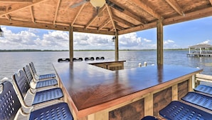 A wooden deck with a bar area, seating, and a view of a lake.