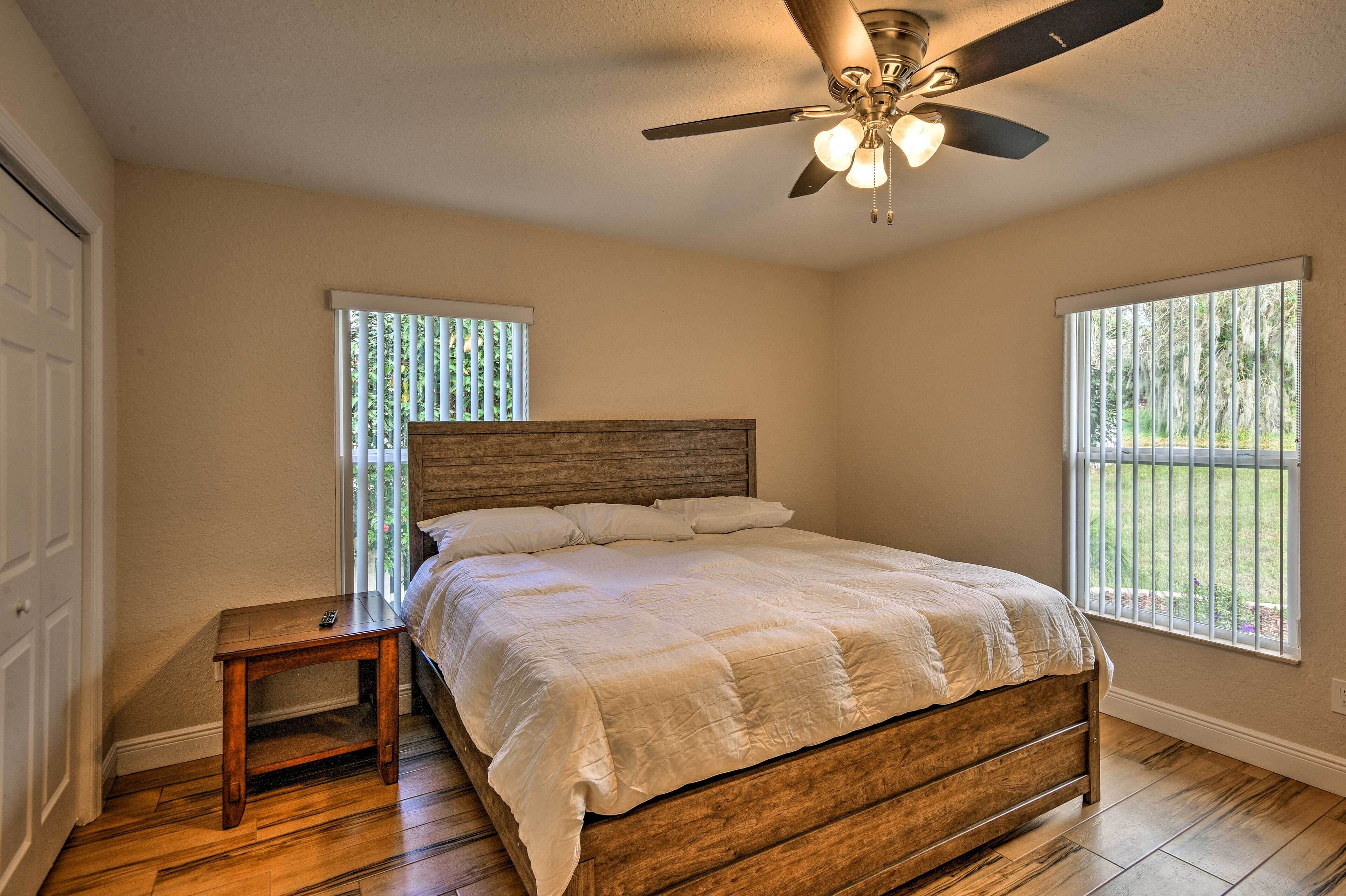 Un dormitorio con cama de madera, ventilador de techo y dos ventanas con persianas.