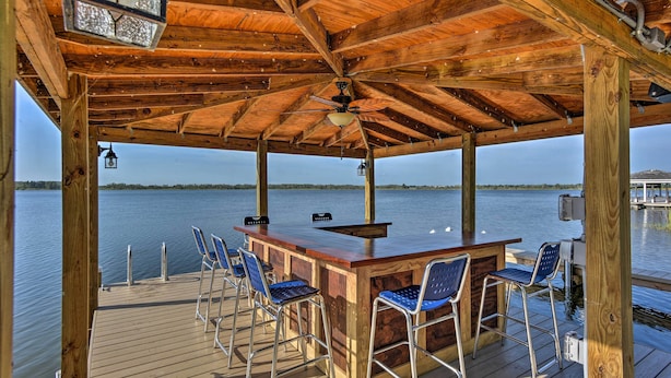 A wooden deck with a bar area, chairs, and a view of the water.