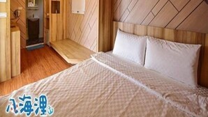 A hotel room with a wooden headboard, a bed with white bedding, a small bathroom with a sink, and a wooden floor. - Bahile (Liuqiu)