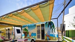 A recreational vehicle with a colorful mural, a covered patio area, and a small table and bench set. - Bahile (Liuqiu)