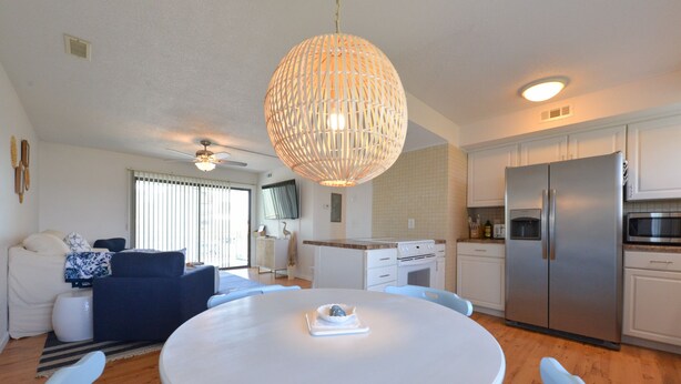 A modern kitchen with white cabinets, a stainless steel refrigerator, and a dining area with a round table and chairs. - Carolina Marsh Hideaway (Carolina Beach)