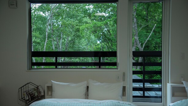A bedroom with a large window, a bed with white bedding, and a small bedside table. - HOTEL BOTH - Hostel (Shari)