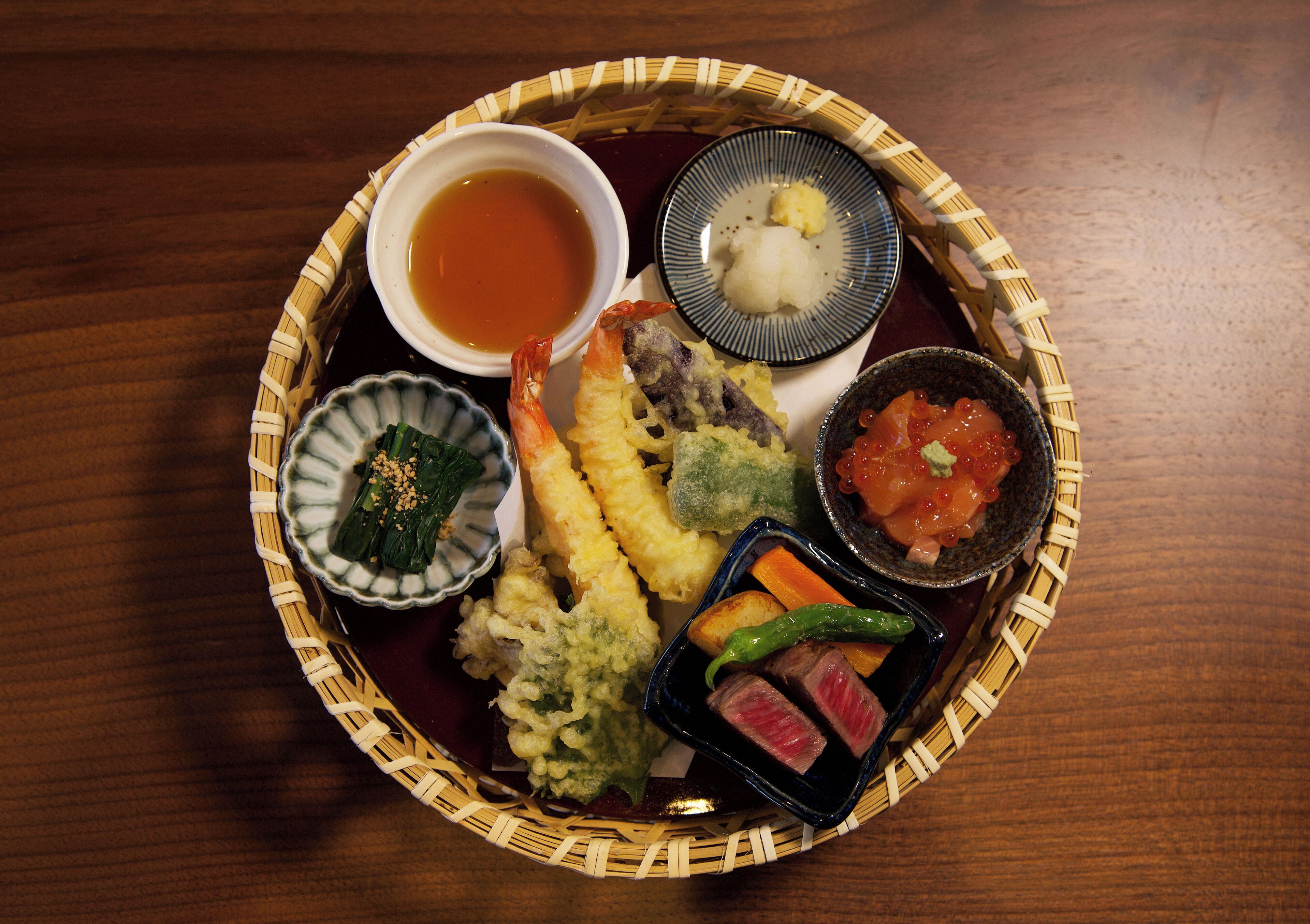 A traditional Japanese meal with various dishes including tempura, sashimi, and a small bowl of soup.